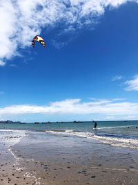 Person paragliding on beach against sky
