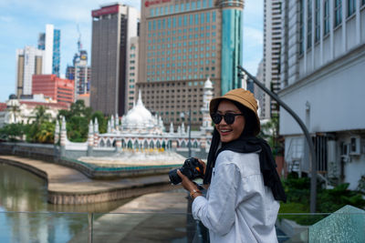 Young woman photographing with mobile phone standing in city