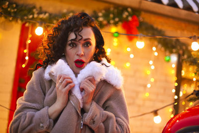 Portrait of smiling young woman standing against illuminated christmas tree at night