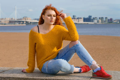 Young red-haired girl in yellow sweater and jeans. pretty woman sits