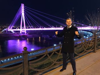 Portrait of man standing on illuminated bridge at night