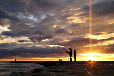 Silhouette of people fishing at sunset