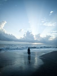 Silhouette woman standing at beach against cloudy sky