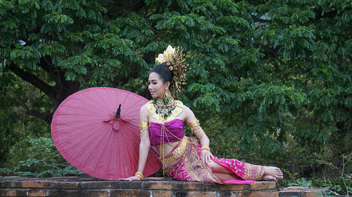 Young woman in traditional clothing with umbrella sitting at forest