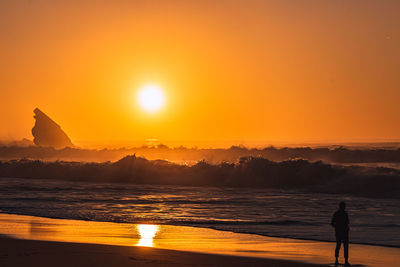 Silhouette man standing on beach against sky during sunset