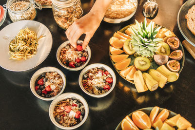 Hand of woman picking up berry from breakfast bowl arranged on table