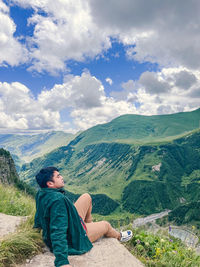 Rear view of woman sitting on mountain against sky