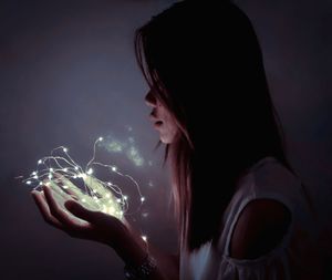 Side view of young woman holding illuminated lights in darkroom