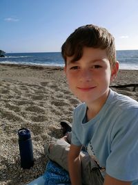 Portrait of boy sitting on shore at beach against sky