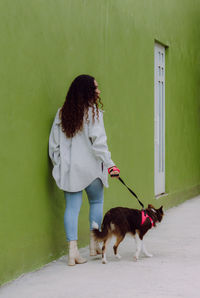 Back view of female owner walking with border collie dog along wet pavement in city