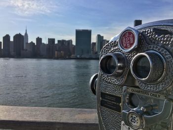 Close-up of coin-operated binocular by hudson river against sky in city