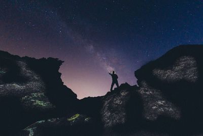 Low angle view of silhouette person standing on rock against sky