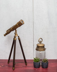 Close-up of telescope and plants on table against wall