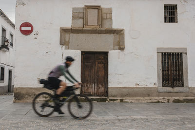 Mature man cycling in front of old house