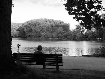 Rear view of people sitting on bench by lake