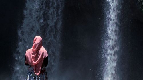 Rear view of man with umbrella at night during rainy season