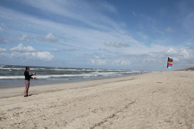 Full length of man holding parasail at beach against sky