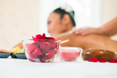 Close-up of petals in bowl with cropped hands of masseuse giving massage to young woman relaxing at spa