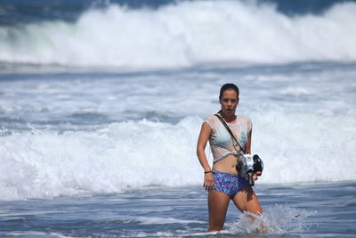 Woman wearing bikini standing in sea while holding camera
