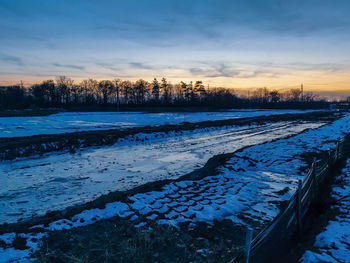 Snow covered field against sky during sunset