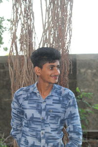 Portrait of young man standing against tree trunk