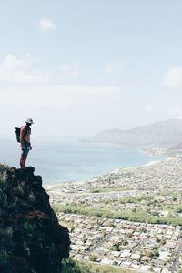 Man standing on cliff by sea against sky