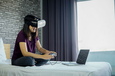 Woman using virtual reality simulator while playing video game on bed