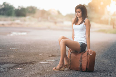 Young woman sitting over suitcase on road
