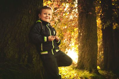 Portrait of smiling boy standing by tree in forest