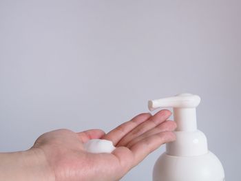 Close-up of hand holding bottle against white background