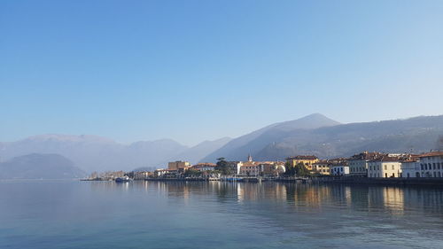 Buildings by sea against clear blue sky