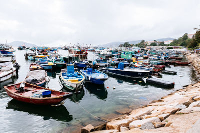 Fishing boats moored at harbor in city against sky