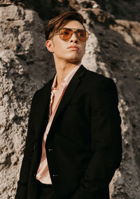 Fashionable young man looking away while standing against rock