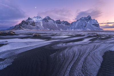 Spectacular nordic scenery of calm frozen lake near rocky vestrahorn mountain with snowy peaks during colorful sunset at stockness beach, iceland