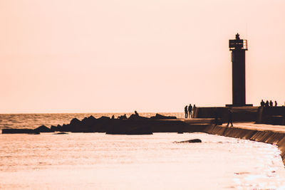 Lighthouse by sea against clear sky during sunset