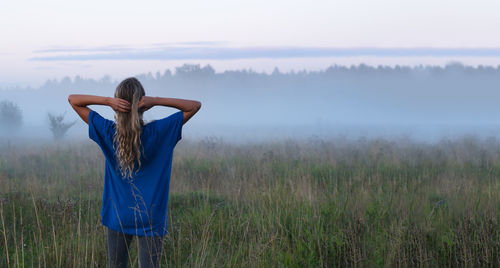 A girl in a blue t-shirt walks through a field with fog at sunset. fog or mist. copy space.