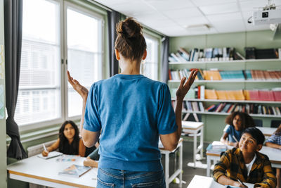 Rear view of female teacher with hair bun teaching group of elementary students in classroom at school