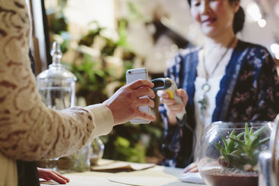 Midsection of customer holding mobile phone while owner scanning qr code in plant shop