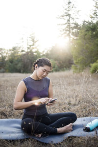 Woman listening music while using smart phone on exercise mat at field