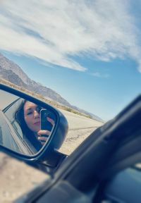 Young woman with mobile phone reflecting on side-view mirror