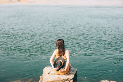 Rear view of woman sitting on rock by sea