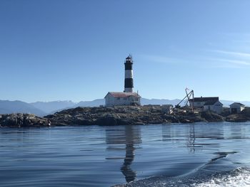Lighthouse by sea against buildings against clear sky