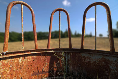 Close-up of rusty metal railing on field against sky