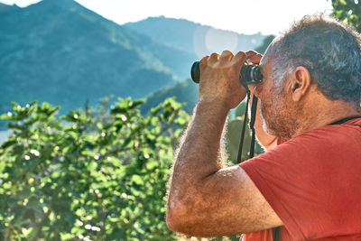 Rear view of tourist man looking through binoculars at the mountains view. hiking, unity with nature