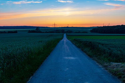 Empty road amidst field against sky during sunset