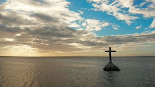 Catholic cross in sunken cemetery in the sea at sunset. 