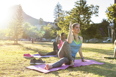 Female friends practicing fish posture on exercise mats against sky in park during sunny day