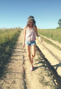 Young woman walking on pathway by field against sky