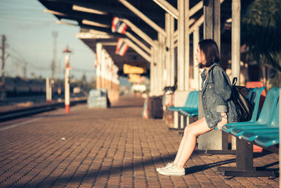 Side view of young woman sitting at railroad station