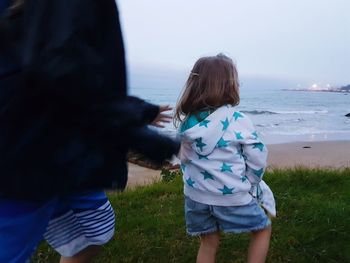 Rear view of girl with brother standing on grassy field at beach against sky